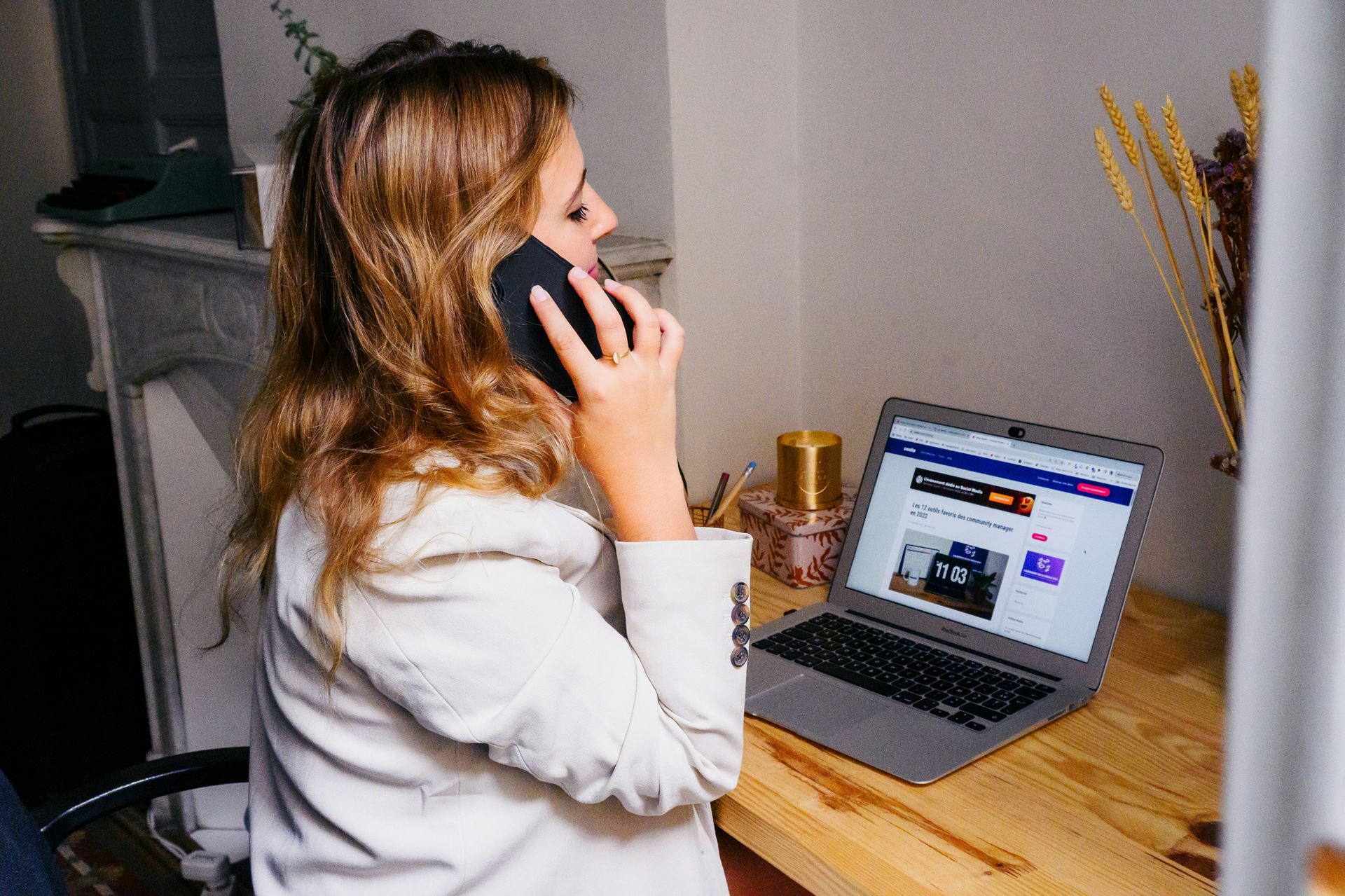 A woman sitting with a laptop and having a phone call on a mobile phone.