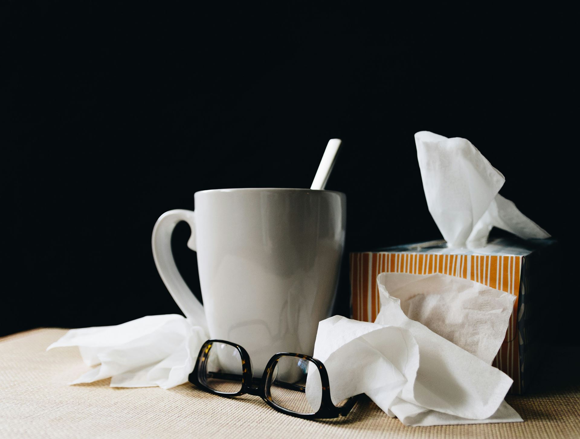 An image of a mug with a spoon, a box of tissues and glasses, indicating they are next to the bed of someone who is unwell