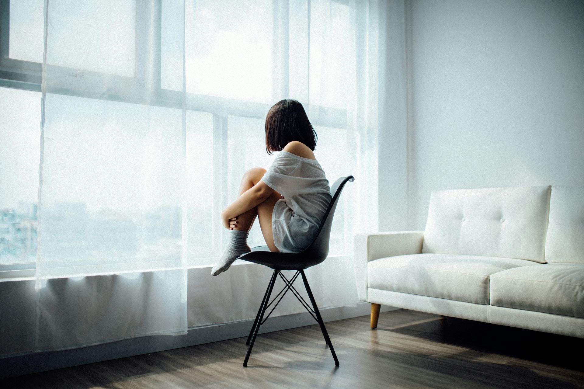 A person sitting on a chair and looking out of a large window